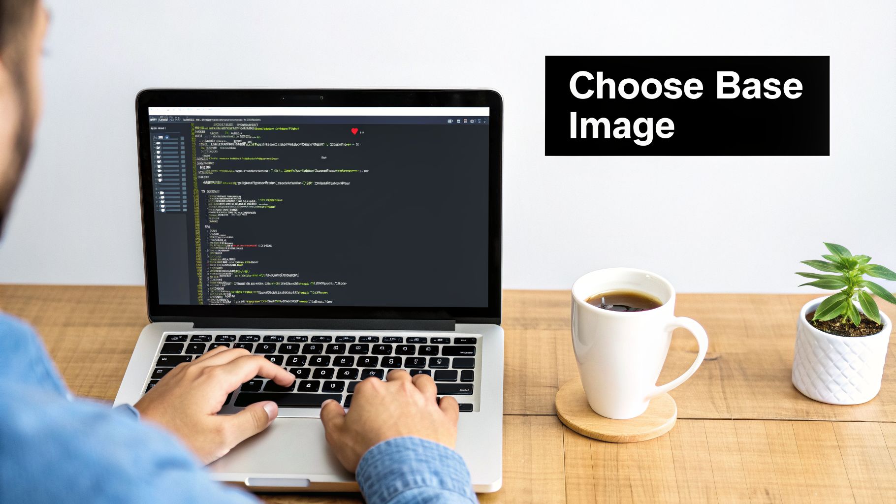 A person coding on a laptop with a coffee mug and a small plant on a light wooden desk.
