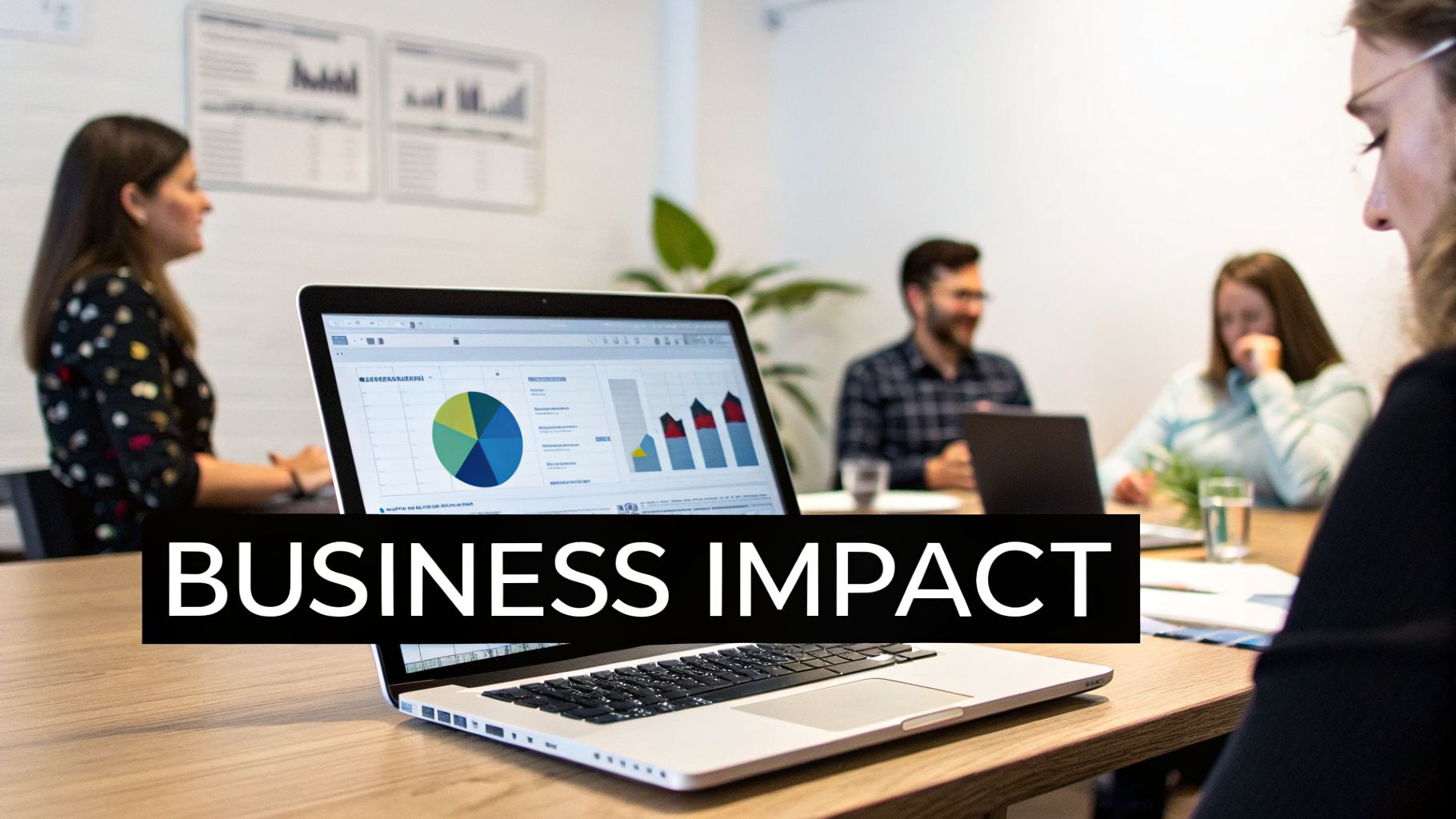 A laptop on a table displays business impact charts during a meeting with colleagues.