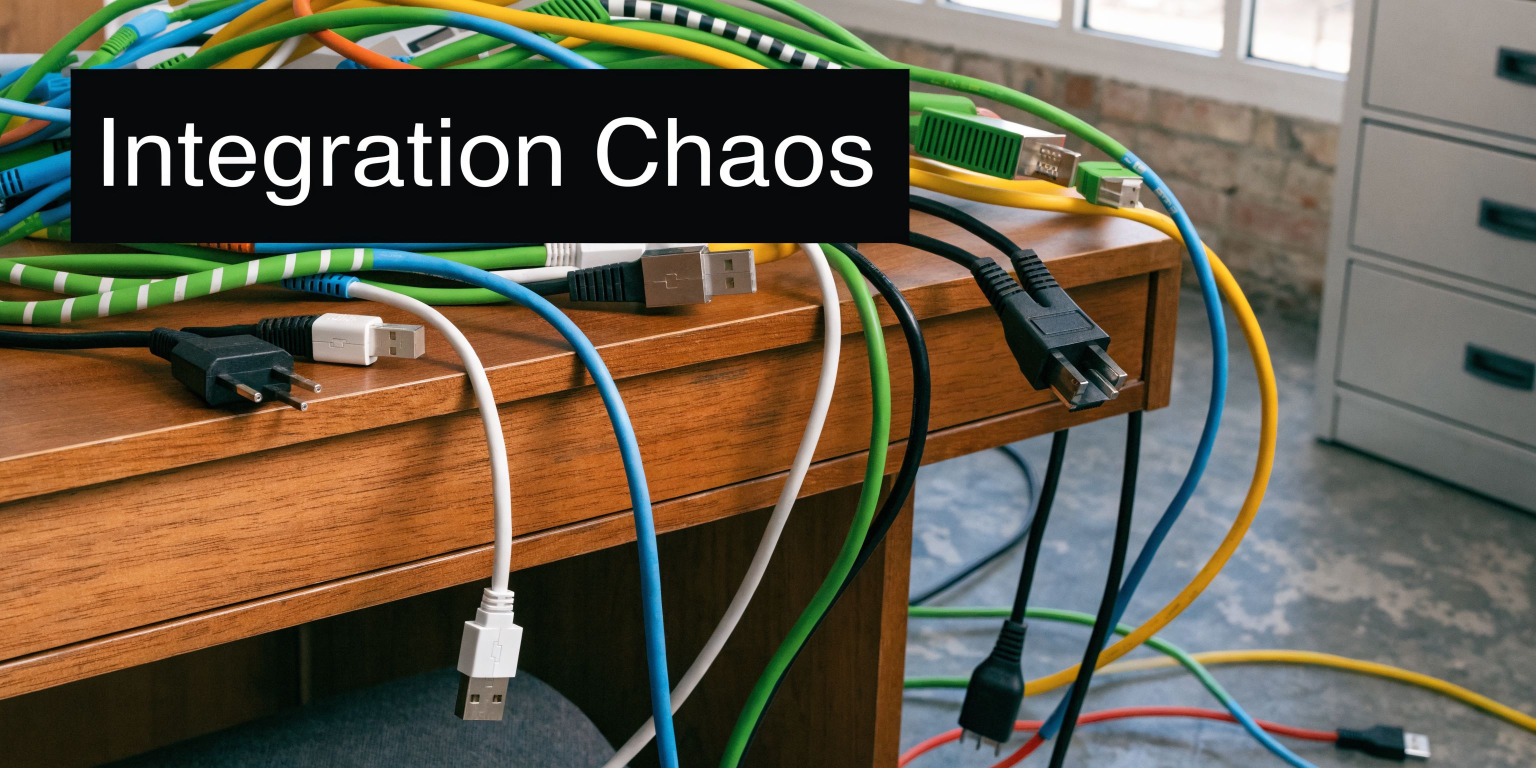 A chaotic mess of colorful tangled computer cables piled on a wooden office desk representing technical integration.