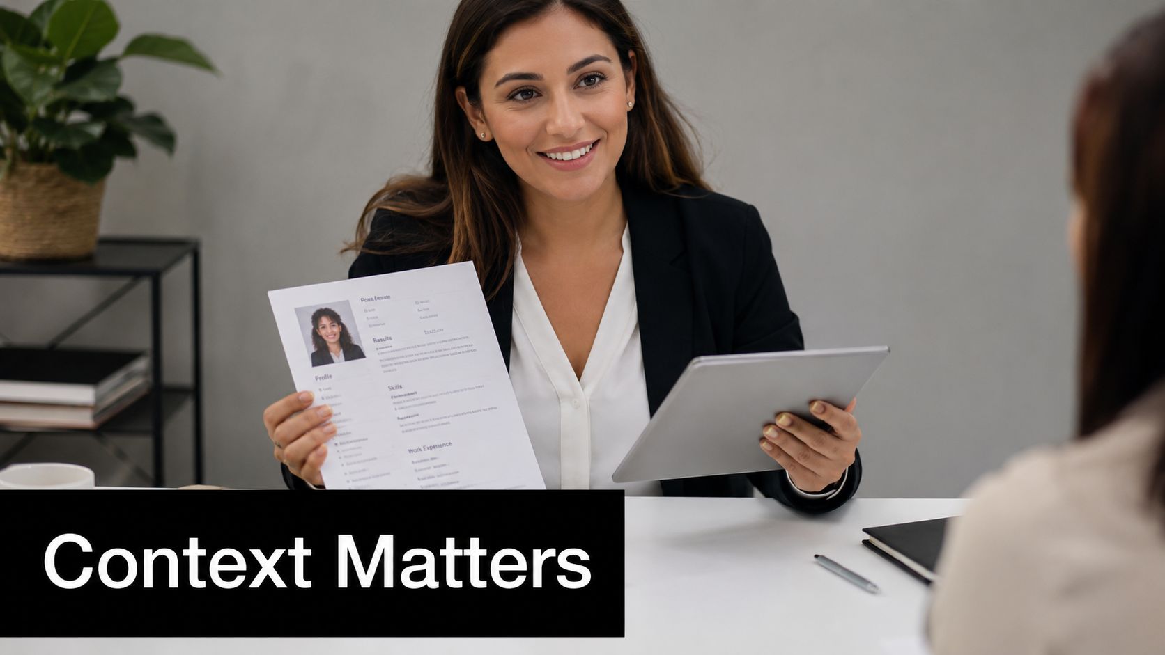 A professional woman in a business suit holding a resume while interviewing a job candidate in office.